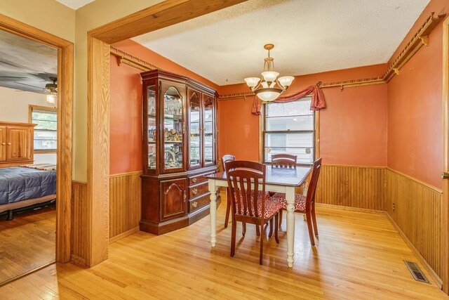 2816 29th Ave NE, Saint Anthony, MN 55418 - dining room featuring a wainscoted wall, light wood finished floors, a chandelier, wood walls, and a textured ceiling
