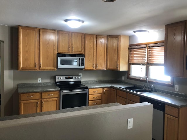1304 13th Ave N, Moorhead, MN 56560 - kitchen featuring stainless steel appliances, a sink, brown cabinetry, and dark countertops