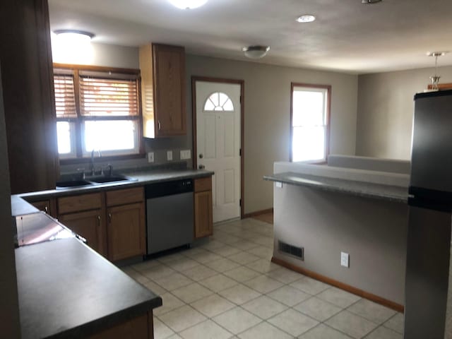 1304 13th Ave N, Moorhead, MN 56560 - kitchen with stainless steel appliances, a sink, brown cabinets, light tile patterned floors, and baseboards