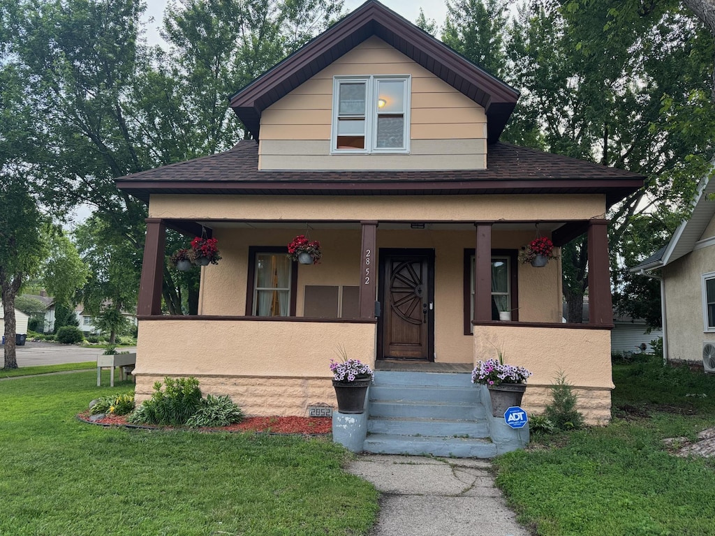 2852 36th Ave S, Minneapolis, MN 55406 - view of front of property with covered porch, a front yard, roof with shingles, and stucco siding