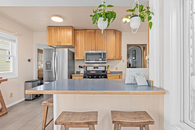 1391 Jefferson Ave, Saint Paul, MN 55105 - kitchen with stainless steel appliances, a peninsula, light tile patterned floors, a breakfast bar area, and light brown cabinetry