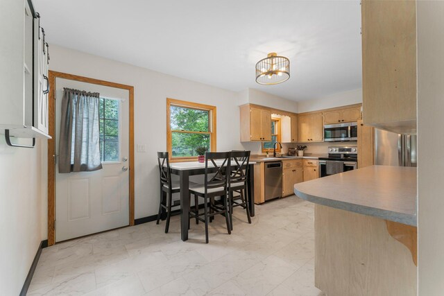 713 9th St NW, Buffalo, MN 55313 - kitchen with stainless steel appliances, light marble finish flooring, light brown cabinets, a chandelier, and baseboards