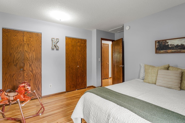 713 9th St NW, Buffalo, MN 55313 - bedroom with light wood-style flooring, multiple closets, attic access, baseboards, and a textured ceiling