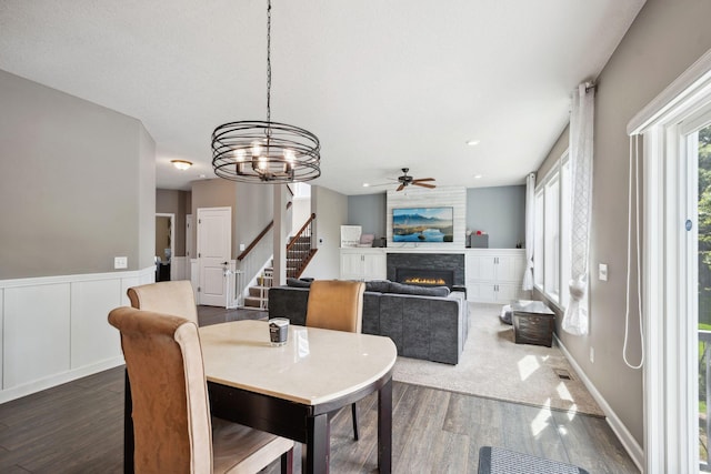 4847 Ashton Curv, Woodbury, MN 55129 - dining space featuring dark wood finished floors, a lit fireplace, ceiling fan, stairs, and a chandelier