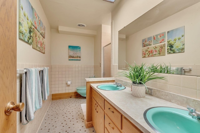 1276 13th Ave N, Saint Cloud, MN 56303 - bathroom featuring double vanity, tile walls, a shower, toilet, and a wainscoted wall