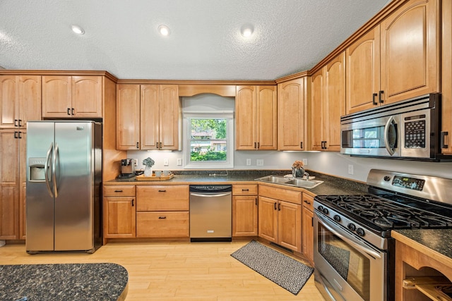 2445 Indian Way N, Saint Paul, MN 55109 - kitchen with stainless steel appliances, a sink, dark countertops, a textured ceiling, and light wood-type flooring