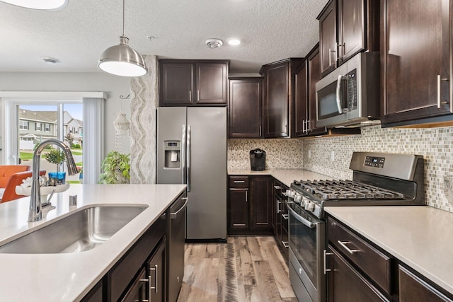 8061 Abercrombie Ln, Woodbury, MN 55129 - kitchen featuring stainless steel appliances, a sink, light wood finished floors, hanging light fixtures, and a textured ceiling