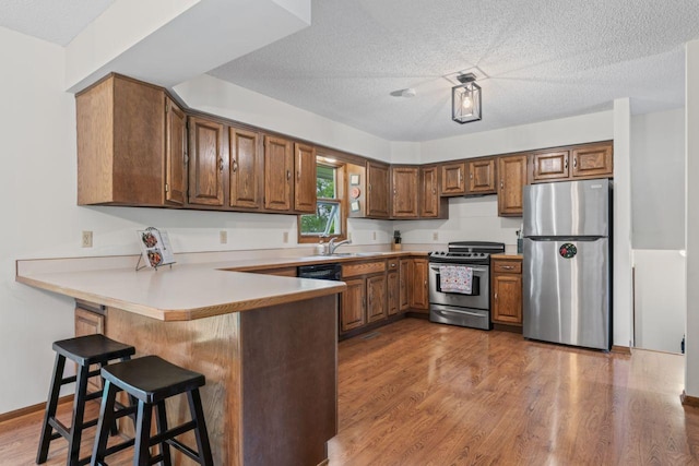 1719 Buckingham Path, Faribault, MN 55021 - kitchen with appliances with stainless steel finishes, a peninsula, a kitchen breakfast bar, wood finished floors, and brown cabinets