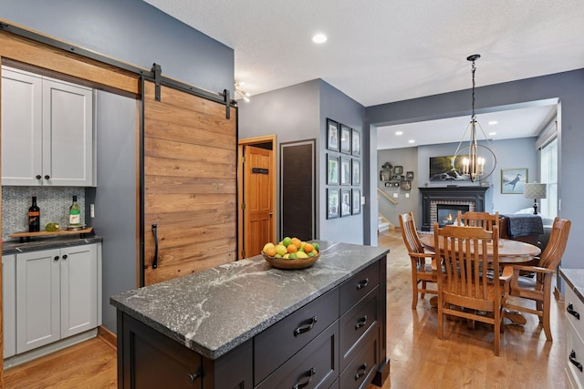 2392 Molnau Ct, Chaska, MN 55318 - kitchen featuring a brick fireplace, light wood-style floors, decorative light fixtures, dark stone counters, and backsplash