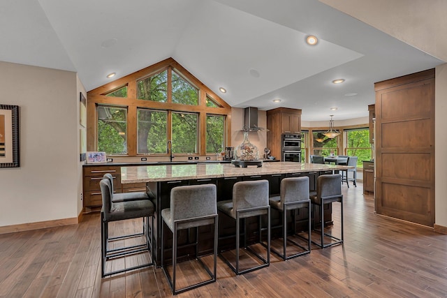 27806 Sundance Ln, Cold Spring, MN 56320 - kitchen with wall chimney exhaust hood, double wall oven, a spacious island, vaulted ceiling, and light stone countertops