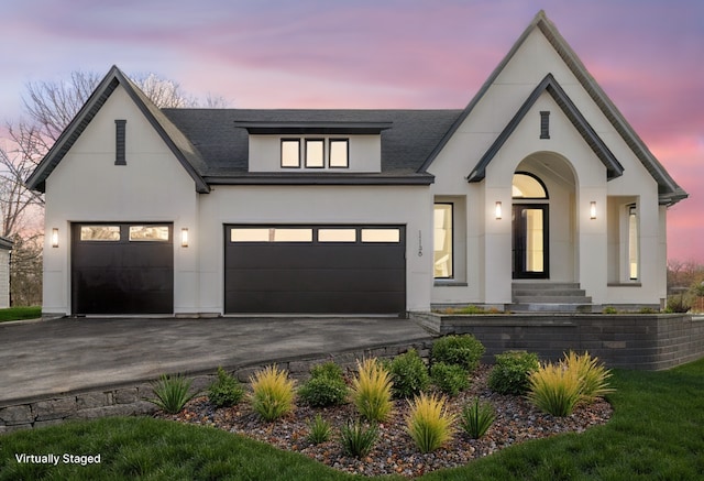french country home with stucco siding, asphalt driveway, an attached garage, and roof with shingles