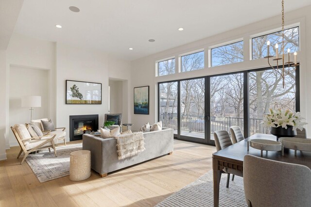 living area featuring a glass covered fireplace, light wood-type flooring, a towering ceiling, and recessed lighting