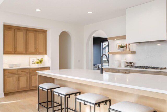 kitchen featuring stainless steel gas stovetop, decorative backsplash, light countertops, a breakfast bar, and recessed lighting