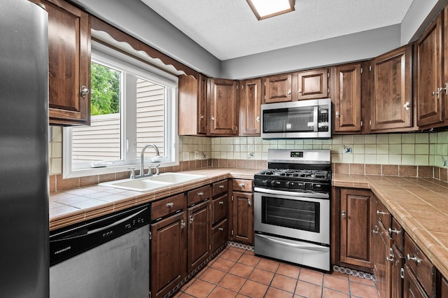 6331 Saint Croix Trl N, Stillwater, MN 55082 - kitchen with appliances with stainless steel finishes, a sink, tile countertops, decorative backsplash, and light tile patterned flooring