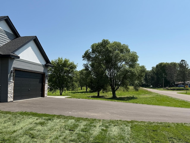 3309 171st Ave NE, Ham Lake, MN 55304 - view of side of property with a garage, a yard, roof with shingles, stone siding, and asphalt driveway