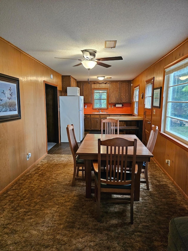 27042 Bluebill Point Rd, Garrison, MN 56450 - dining area featuring wooden walls, a textured ceiling, a ceiling fan, dark carpet, and baseboards