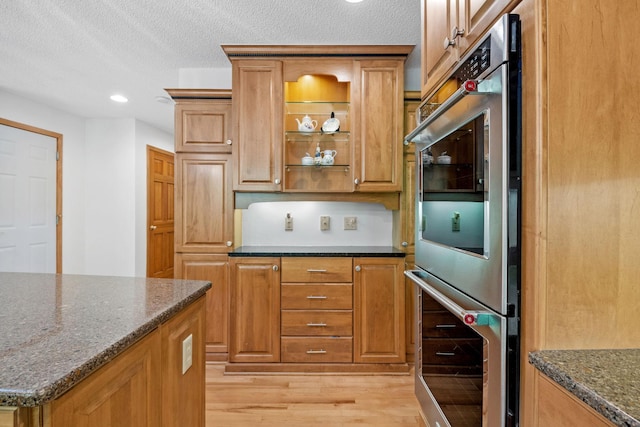 6136 Arctic Way, Edina, MN 55436 - kitchen with double oven, light wood-type flooring, dark stone counters, a textured ceiling, and brown cabinets