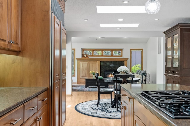 6136 Arctic Way, Edina, MN 55436 - kitchen featuring gas cooktop, light wood finished floors, glass insert cabinets, a tiled fireplace, and dark stone countertops