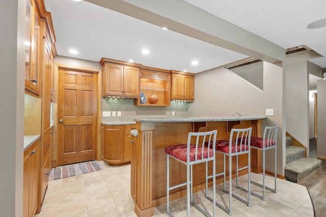 6136 Arctic Way, Edina, MN 55436 - kitchen featuring a kitchen breakfast bar, a peninsula, recessed lighting, brown cabinets, and light stone counters