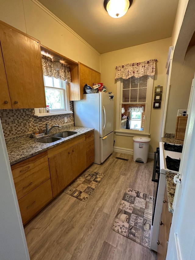 502 1st Ave SE, Baudette, MN 56623 - kitchen with a sink, white appliances, brown cabinets, light wood finished floors, and tasteful backsplash
