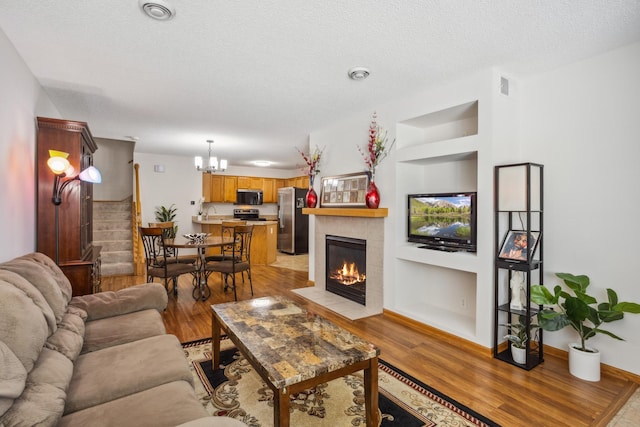 16480 Elm Creek Ln, Lakeville, MN 55044 - living room with light wood-type flooring, built in shelves, a chandelier, a textured ceiling, and a tiled fireplace