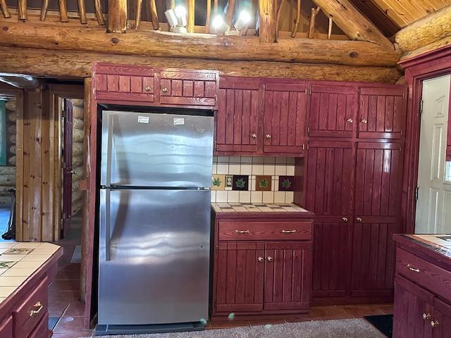 3547 Norway Ln, Ely, MN 55731 - kitchen with freestanding refrigerator, tile counters, log walls, backsplash, and dark tile patterned flooring