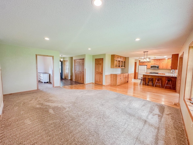 731 Grove Ave, Bird Island, MN 55310 - unfurnished living room with light carpet, recessed lighting, a textured ceiling, a chandelier, and baseboards