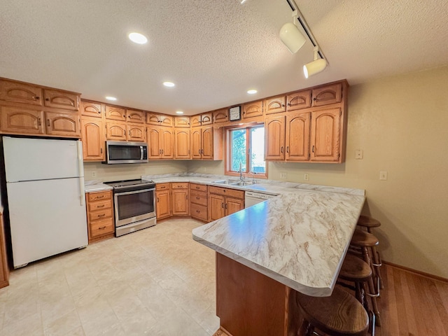 731 Grove Ave, Bird Island, MN 55310 - kitchen featuring stainless steel appliances, a peninsula, track lighting, a textured ceiling, and a kitchen breakfast bar