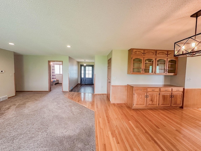 731 Grove Ave, Bird Island, MN 55310 - kitchen with a textured ceiling, light wood finished floors, glass insert cabinets, brown cabinetry, and a wainscoted wall