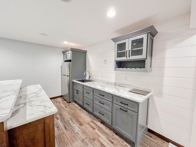 731 Grove Ave, Bird Island, MN 55310 - kitchen featuring gray cabinets, a sink, freestanding refrigerator, light wood-type flooring, and wooden walls