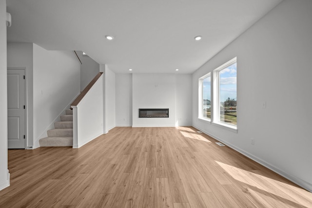 7150 Large Ave NE, Otsego, MN 55301 - unfurnished living room with light wood-type flooring, stairway, a glass covered fireplace, baseboards, and recessed lighting