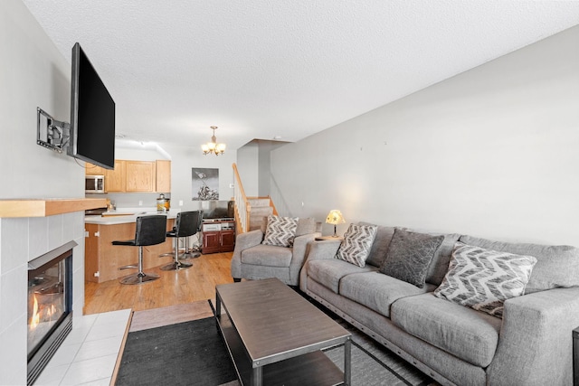 20616 Erin Way Unit 74, Farmington, MN 55024 - living room featuring stairs, a chandelier, light wood-type flooring, a tiled fireplace, and a textured ceiling