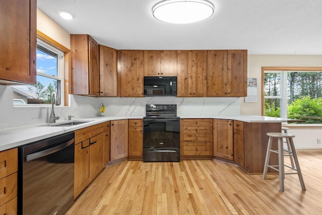 11520 120th St N, Stillwater, MN 55082 - kitchen featuring black appliances, light wood-style flooring, a sink, a peninsula, and brown cabinetry
