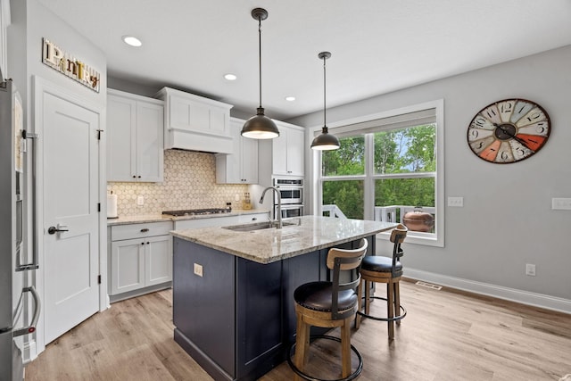 7137 61st St S, Cottage Grove, MN 55016 - kitchen featuring a sink, light wood-style flooring, backsplash, light stone countertops, and a kitchen island with sink