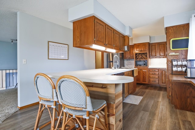 208 Concord St, West Concord, MN 55985 - kitchen featuring a sink, dark wood-style flooring, light countertops, brown cabinetry, and tasteful backsplash