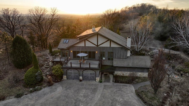 N30732 Square Bluff Rd, Blair, WI 54616 - back of house at dusk featuring a chimney, concrete driveway, a balcony, a garage, and stone siding