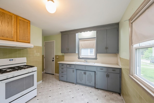3425 Cleveland St NE, Minneapolis, MN 55418 - kitchen featuring white range with gas cooktop, gray cabinets, under cabinet range hood, tile walls, and wainscoting