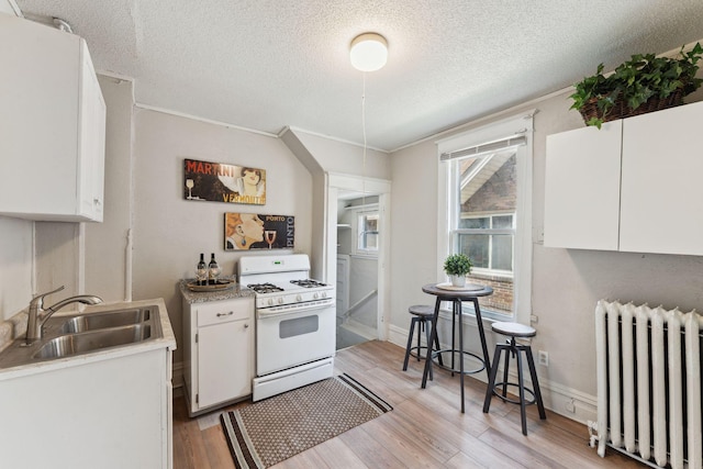 1404 Russell Ave N, Minneapolis, MN 55411 - kitchen featuring radiator, white range with gas stovetop, a sink, white cabinetry, and light countertops
