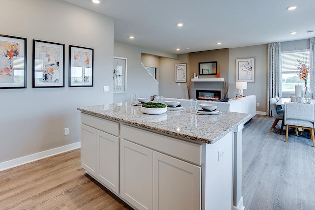 1025 Shoreview Dr, Jordan, MN 55352 - kitchen featuring light wood-type flooring, recessed lighting, baseboards, a glass covered fireplace, and white cabinets
