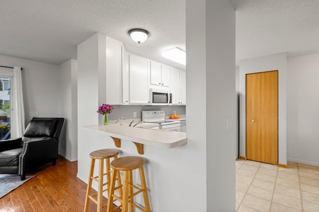 16047 72nd St NE, Otsego, MN 55330 - kitchen featuring stainless steel microwave, white range with electric stovetop, a breakfast bar area, light countertops, and white cabinetry