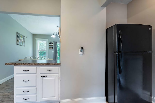 113 7th Ave SE, Elbow Lake, MN 56531 - kitchen with freestanding refrigerator, baseboards, white cabinets, wood finished floors, and a peninsula
