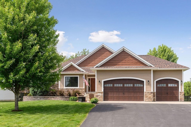227 Maple Ln, Jordan, MN 55352 - craftsman house with an attached garage, asphalt driveway, a front lawn, stone siding, and roof with shingles