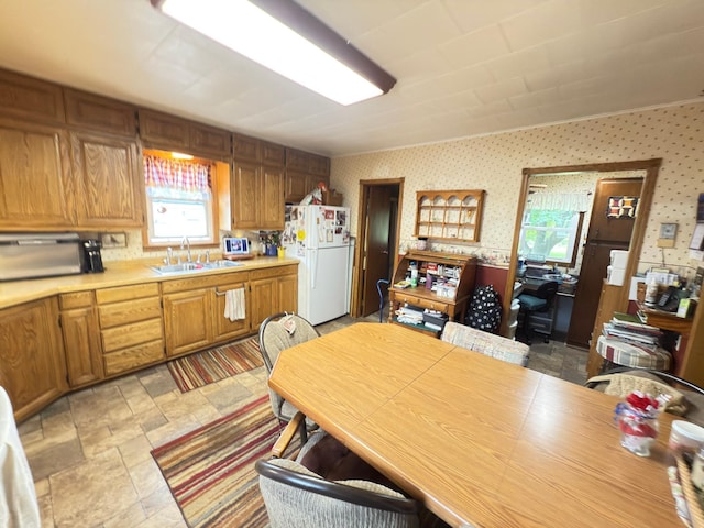 107 3rd Ave, Bellingham, MN 56212 - kitchen featuring freestanding refrigerator, a sink, wallpapered walls, light countertops, and brown cabinetry