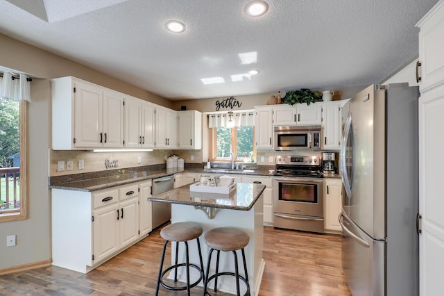 2301 170th Ln NW, Andover, MN 55304 - kitchen with appliances with stainless steel finishes, a sink, light wood-style floors, a center island, and a textured ceiling