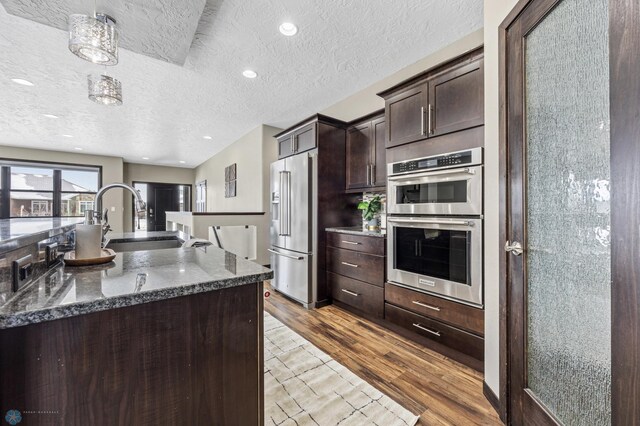 2800 Mcleod Dr E, West Fargo, ND 58078 - kitchen with appliances with stainless steel finishes, dark brown cabinets, a textured ceiling, a sink, and wood finished floors