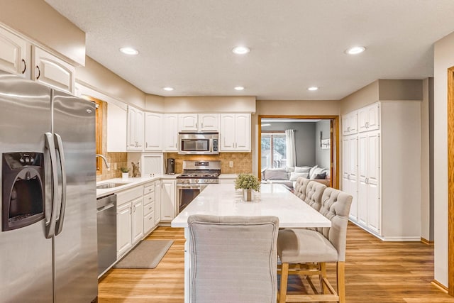 38 Jefferson Ct, Hastings, MN 55033 - kitchen with stainless steel appliances, a sink, white cabinetry, backsplash, and a kitchen breakfast bar