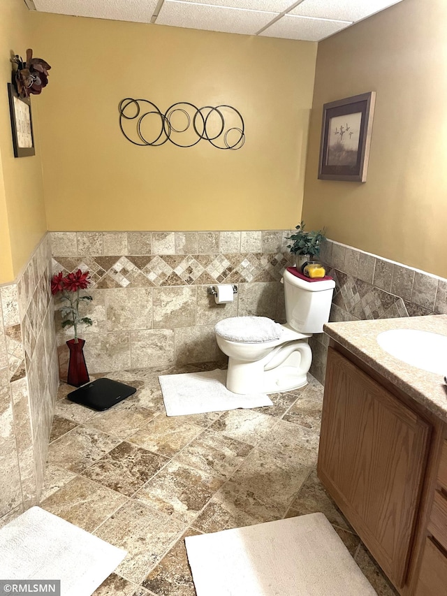 705 Turril St, Le Sueur, MN 56058 - bathroom with tile walls, toilet, vanity, a wainscoted wall, and stone finish flooring