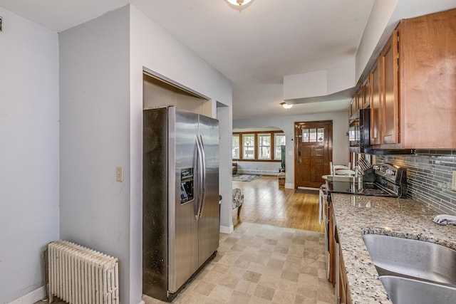 1167 Geranium Ave E, Saint Paul, MN 55106 - kitchen featuring appliances with stainless steel finishes, radiator heating unit, tasteful backsplash, brown cabinets, and baseboards