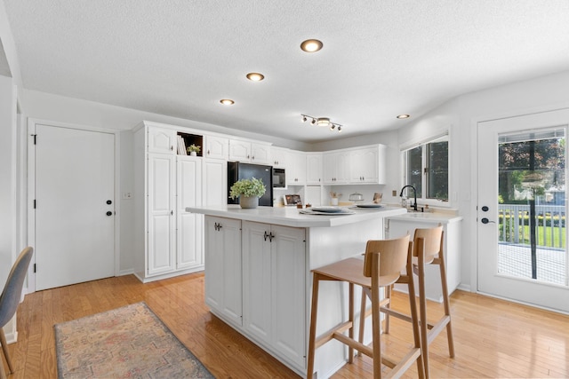6540 Zealand Ave N, Brooklyn Park, MN 55428 - kitchen with black appliances, a kitchen breakfast bar, white cabinetry, light wood-type flooring, and a textured ceiling