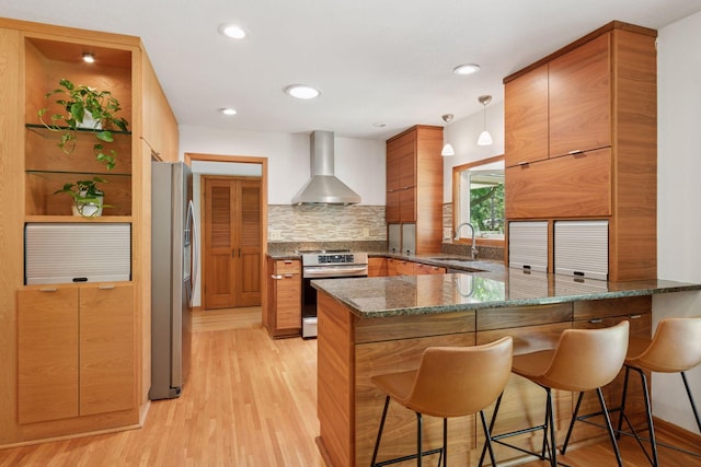 10933 Chowen Ave S, Bloomington, MN 55431 - kitchen with wall chimney range hood, appliances with stainless steel finishes, a peninsula, a sink, and light wood-style floors